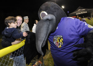 Baltimore Ravens mascot Poe greets Army Staff Sgt. Mark Blakeman, second from left, of Meuse Forest, and his son Ezra, 1, during a Ravens youth football clinic at Fort Meade Monday, Nov. 3, 2014. (Photo by Steve Ruark)